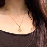 A person wearing a gold pendant necklace featuring a textured geometric shaped pendant with small ruby and diamonds, and a small matching charm with ruby at the side.